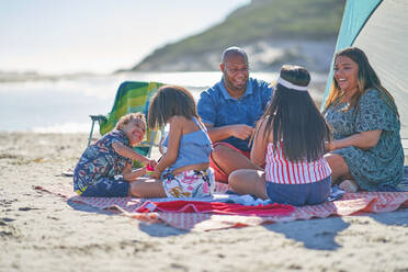 Glückliche Familie auf Picknickdecke am sonnigen Strand - CAIF32369