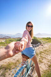 POV happy woman riding bicycle holding hand on sunny beach path - CAIF32372