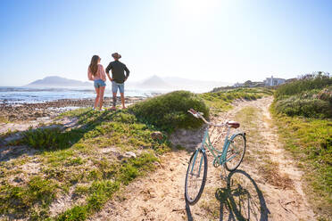 Couple standing on sunny sandy summer ocean beach with bicycle - CAIF32373