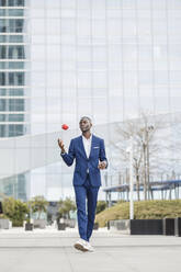 Businessman playing with apple walking on footpath - IFRF01639