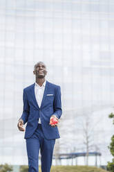 Lächelnder Mann mit Apfel in der Hand vor einem modernen Bürogebäude - IFRF01640
