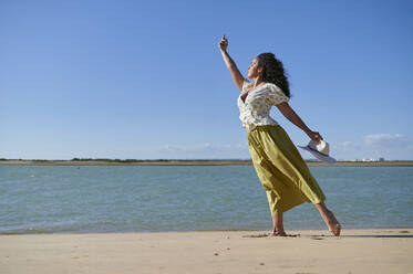 Junge Frau mit erhobener Hand tanzt am Ufer am Strand - KIJF04457