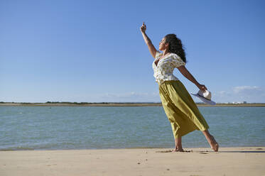 Young woman with hand raised dancing on shore at beach - KIJF04457