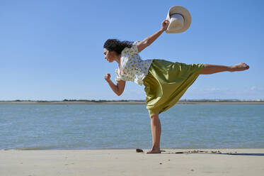 Junge Frau mit Hut in der Hand tanzt am Strand - KIJF04458