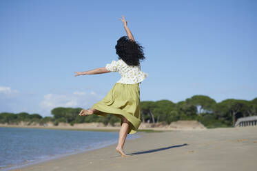 Unbekümmerte Frau tanzt am Strand an einem sonnigen Tag - KIJF04462