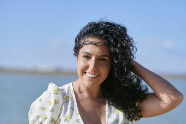 Happy young woman with hand in hair at beach on sunny day - KIJF04464