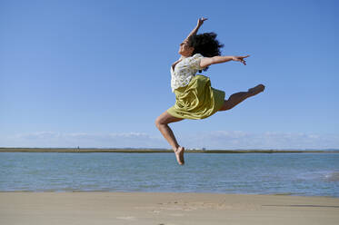 Unbekümmerte junge Frau, die an einem sonnigen Tag am Strand springt - KIJF04468