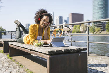 Businesswoman listening music and working on laptop by River Main - UUF25928