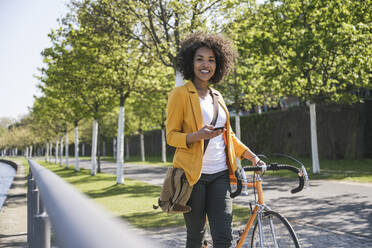 Lächelnde Geschäftsfrau mit Fahrrad auf dem Fußweg - UUF25941