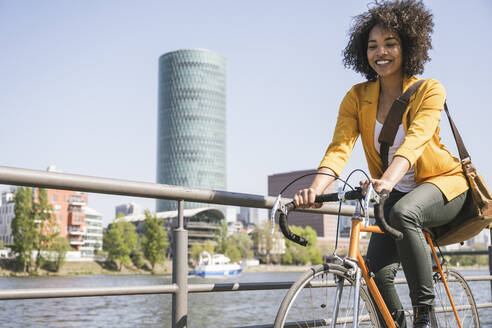 Glückliche Geschäftsfrau fährt an einem sonnigen Tag am Main Fahrrad - UUF25945