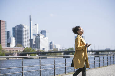 Businesswoman walking by River Main on sunny day - UUF25966