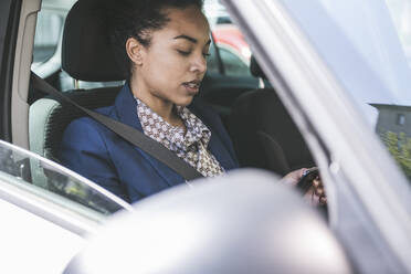 Geschäftsfrau mit Smartphone im Auto sitzend - UUF25968