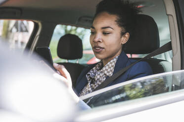 Junge Geschäftsfrau, die im Auto sitzend ein Smartphone benutzt - UUF25970