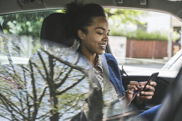 Lächelnde Geschäftsfrau mit Mobiltelefon im Auto sitzend - UUF25971