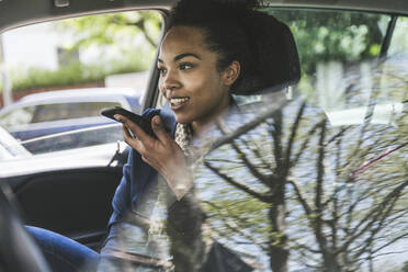 Geschäftsfrau, die im Auto sitzend eine Voicemail über ihr Smartphone sendet - UUF25972