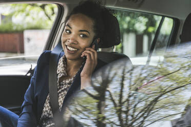 Geschäftsfrau, die im Auto auf einer Autoreise mit einem Mobiltelefon spricht - UUF25973