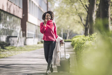 Businesswoman walking with wheeled luggage on footpath - UUF26006