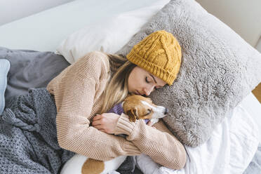 Frau in warmer Kleidung kuschelnd mit Hund im Bett - KMKF01821