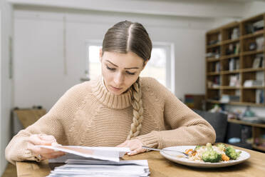 Young woman at lunch sitting at table checking bills - KMKF01828