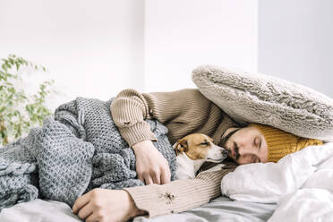 Erschöpfter Mann schläft voll bekleidet im Bett mit Hund - KMKF01835