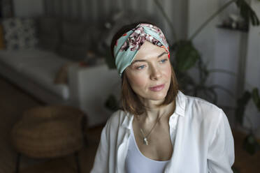 Thoughtful mature woman wearing headband sitting in living room at home - LLUF00493