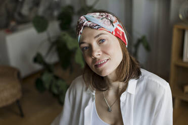 Smiling mature woman with brown hair wearing headband in living room at home - LLUF00496