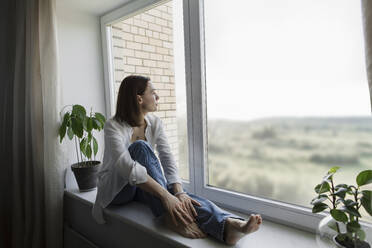 Reife Frau sitzt auf der Fensterbank zu Hause - LLUF00510