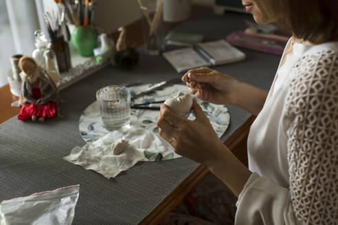 Ältere Frau modelliert Puppen Gesicht sitzen am Tisch zu Hause - LLUF00517