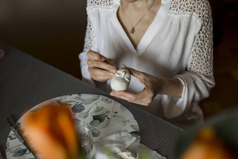 Ältere Frau modelliert Puppengesicht sitzend zu Hause - LLUF00518