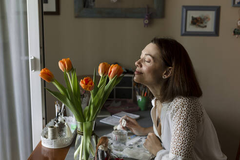 Reife Frau riecht an Tulpenblüten auf dem Tisch zu Hause - LLUF00521