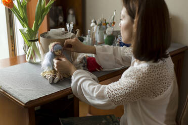 Frau dekoriert handgefertigte Puppe auf Tisch zu Hause - LLUF00523