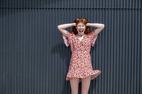 Young woman with head in hands screaming in front of corrugated iron wall - LBF03631