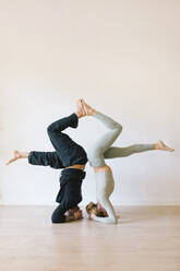 Mann und Frau üben Kopfstand vor einer Wand im Yogastudio - MMPF00044