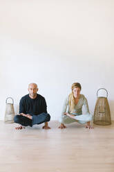 Friends practicing tolasana pose in front of wall at yoga studio - MMPF00047