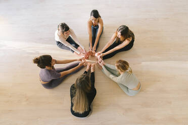 Women sitting in circle touching toes at yoga studio - MMPF00051