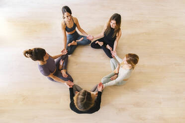 Frauen sitzen im Lotussitz und meditieren im Yogastudio - MMPF00053