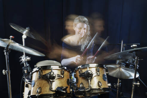 Happy drummer playing drum kit against black background - RNF01344