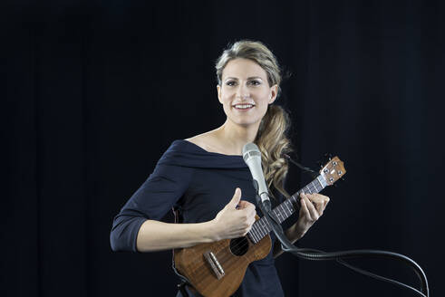 Mature performer playing ukulele against black background - RNF01349