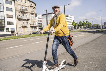 Glücklicher älterer Mann mit elektrischem Tretroller in der Stadt - UUF26010