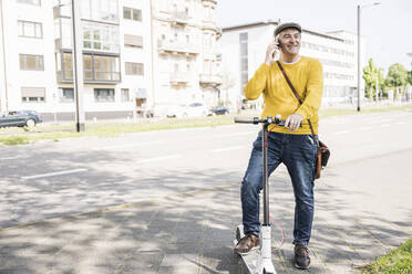 Smiling senior man talking on mobile phone standing with electric push scooter in city - UUF26019