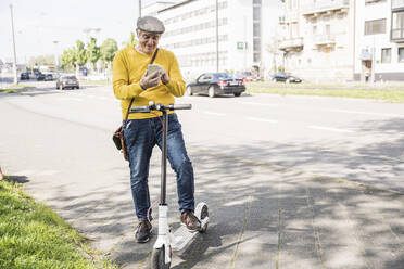 Happy senior man using mobile phone standing with electric push scooter - UUF26020