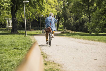 Älterer Mann fährt mit dem Fahrrad auf dem Fußweg im Park - UUF26025