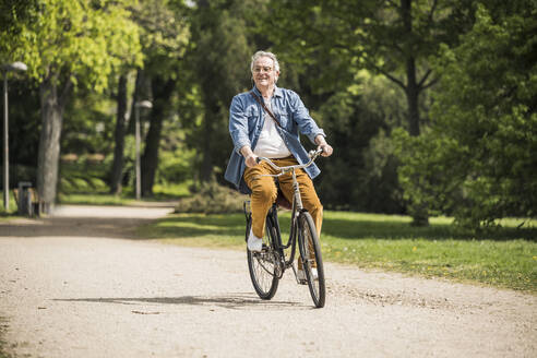 Lächelnder älterer Mann auf dem Fahrrad im Park an einem sonnigen Tag - UUF26026