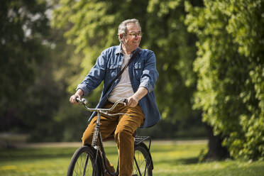 Happy man wearing eyeglasses riding on bicycle at park on sunny day - UUF26030