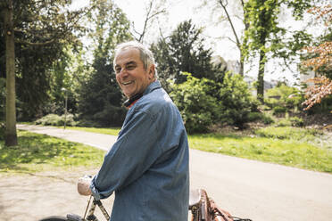 Glücklicher älterer Mann auf dem Fahrrad an einem sonnigen Tag - UUF26061