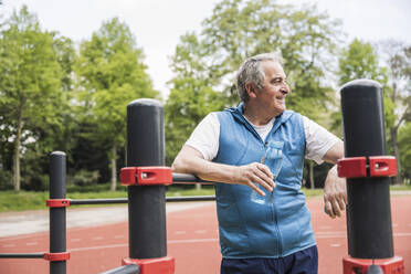 Glücklicher älterer Mann mit Wasserflasche an der Gymnastikstange - UUF26062