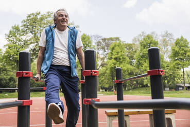 Glücklicher aktiver älterer Mann, der im Park an einem Gymnastikbalken trainiert - UUF26066