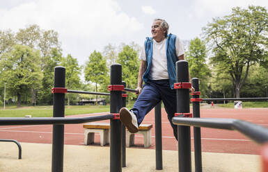 Lächelnder aktiver älterer Mann, der im Park am Gymnastikbalken trainiert - UUF26067
