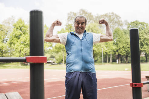 Happy senior man flexing muscles at park - UUF26069