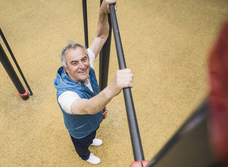 Smiling senior man holding gymnastics bar at park - UUF26070